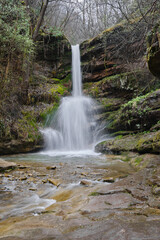 Fototapeta premium Powerful water of a waterfall splashing down the wet, vivid green moss covered rocks of a cliff during early spring
