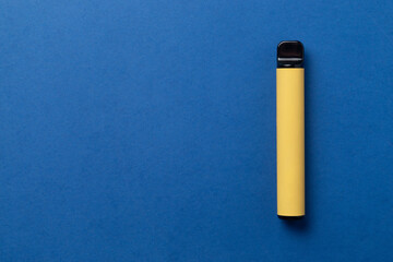 Disposable e-cigarette in yellow color on blue isolated background. The concept of modern smoking, vaping and nicotine. Top view