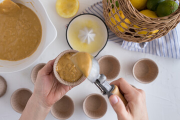 Bakery cup just filled with a muffin batter by a woman hand using a blurred ice cream scoop.