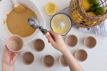 Right woman hand holding an ice cream scoop ready to fill it with a muffin batter and holding an empty bakery cup with the left hand.