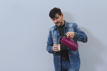 Hombre cebando mate con termo color bordó vestido con denim en fondo aislado celeste © Guillermo