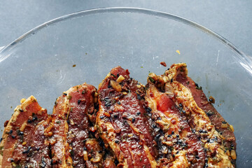 Korean style marinated pork belly slices in a glass bowl, close up. Meat industry product.