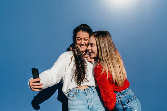couple of friends, one blonde and the other brunette, taking a picture with their cell phone