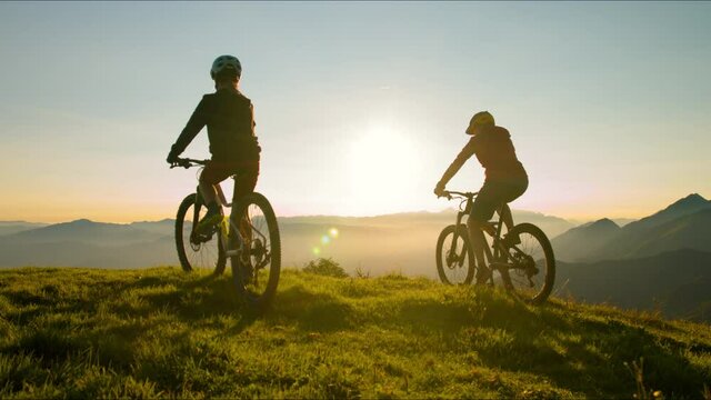 Two cheerful woman lifts his bicycle above his head at sunset after a winning mountain biking ride.