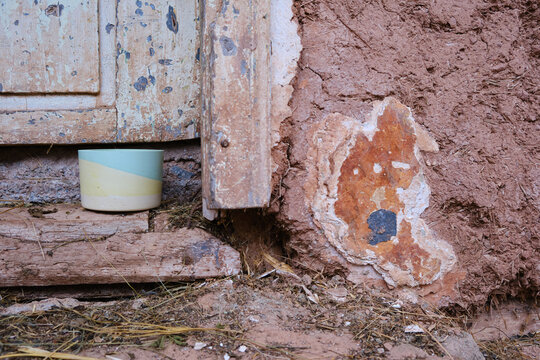 Selective focus on colorful plaster pot for cactuses in front of an old, rustic, wooden door of a house made from mud and some hay on the ground