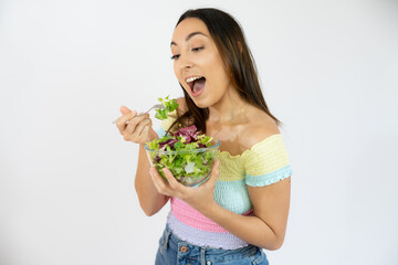 Portrait of a happy playful woman eating fresh salad from a bowl isolated over white background