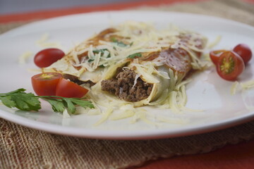 Pancakes with meat, in tomato sauce and cheese, with cilantro and grated cheese on top, and some cherry tomatoes on the plate.