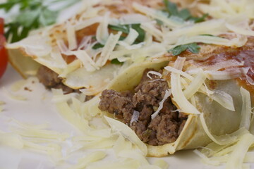 Pancakes with meat, in tomato sauce and cheese, with cilantro and grated cheese on top, and some cherry tomatoes on the plate.