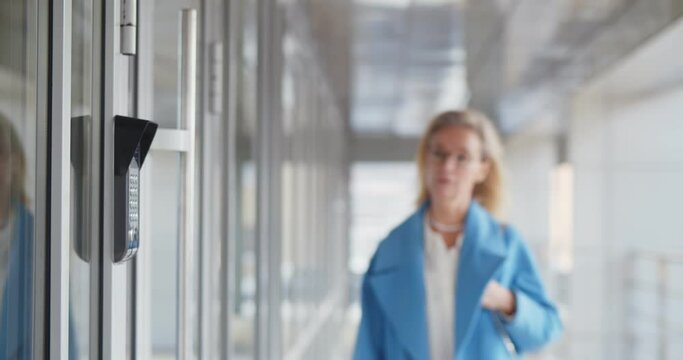 Mature woman scanning fingerprint on alarm system entering business center