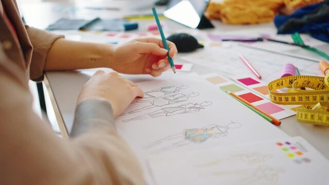 Close up of left-handed fashion designer sketching clothes collection, working at workshop, tracking shot, slow motion