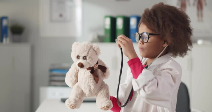 Cute small child pretending to be doctor examining teddy bear with stethoscope