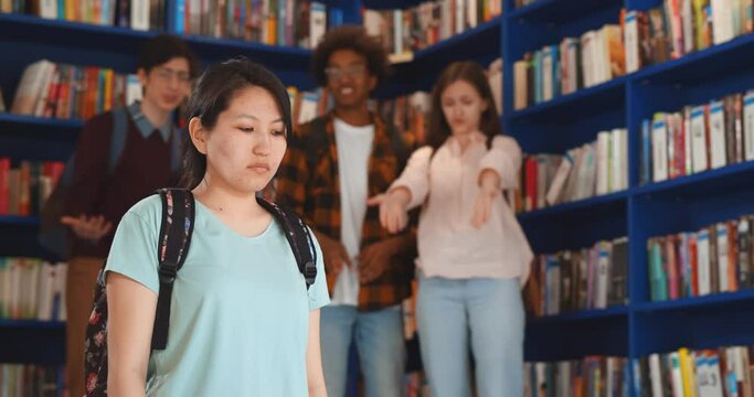 Diverse students bullying and laughing at sad asian young woman in library