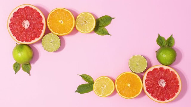 Fresh citrus fruits and green leaves make frame arrangement with copy space on pastel pink background. Stop motion