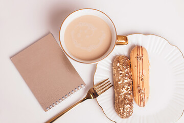 Beautiful golden colored eclairs on plate, knife and fork, cup of coffee, with copy space