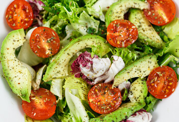 Fresh green salad with avocado, tomatoes, goat cheese in big white bowl on wooden tray. Vegan salad with green mix leaves  and vegetables. Top view on gray table. Healthy vegetarian food. Close up