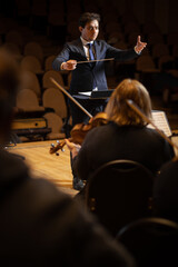 Conductor of symphony orchestra with performers in background in concert hall
