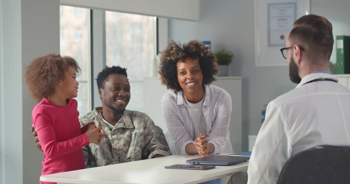 Afro-american wounded soldier with wife and daughter visiting practitioner in clinic