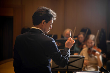 Conductor of symphony orchestra with performers in background in concert hall