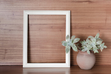 Empty white frame with succulent plant on wooden background.