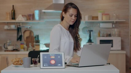 Woman using voice activated smart wireless lighting app on tablet turning on the bulbs in house with modern software working at laptop. Person controlling ambience light with future technology - Powered by Adobe