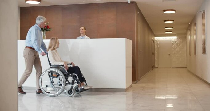 Female receptionist greeting mature man with disabled wife in wheelchair