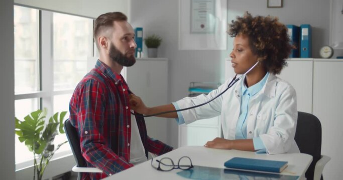 Female doctor examining patient heart beat with stethoscope in office.