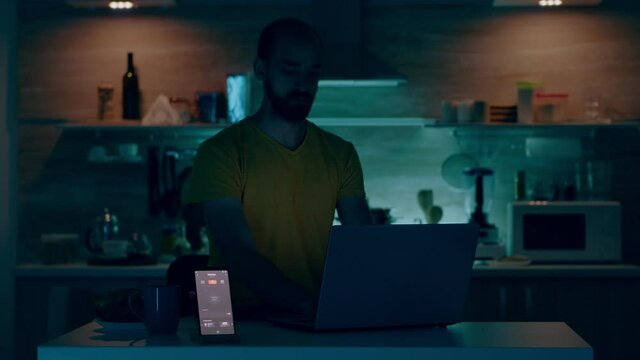 Man working from house with automation lighting system, sitting in kitchen turning on the lights using voice command to smart home application on smartphone. Person monitoring light with wifi gadget