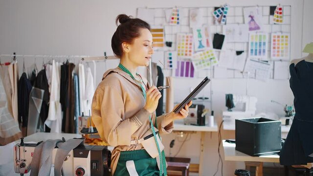 Cheerful female fashion designer making online research about trends on tablet, looking for inspiration at workshop