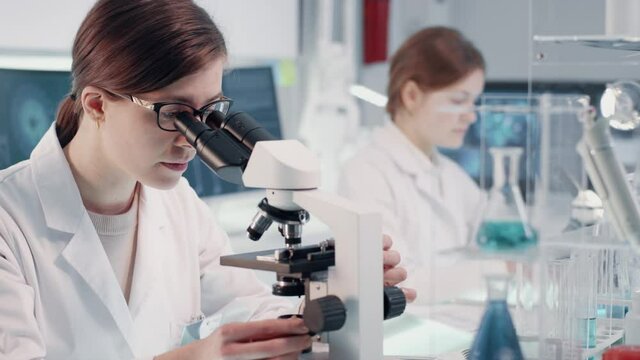 Female scientists working in laboratory. Studying medical samples with microscopes and using computers. Virus and human skeleton models on screens