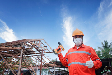 An Asian man, 35, wears protective drill gloves, a carpenter uses an electric drill to build a wooden house