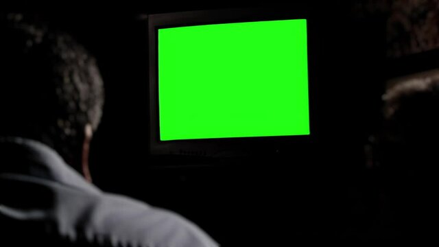 Men Watching Television Set with Green Screen in a Dark Room. You can replace green screen with the footage or picture you want. You can do it with “Keying” effect in After Effects.