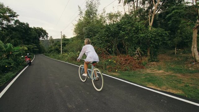 Biking road trip. The woman on blue bike in white clothes on forest road. The girl ride on bicycle. Cycling Cycle Fix. Asia Thailand ride tourism.