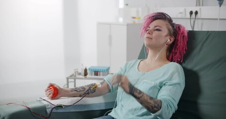 Female patient listening to music while giving her blood in hospital room - Powered by Adobe