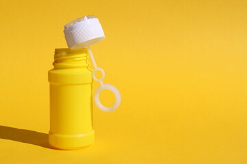 Yellow bottle for soap bubbles stands on yellow background with place for text
