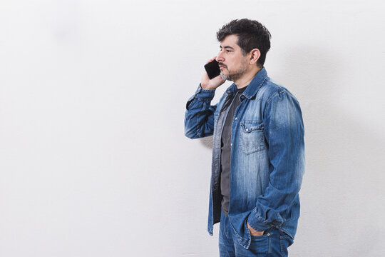 Hombre morocho con camisa, de perfil hablando por tel&eacute;fono sobre fondo blanco 