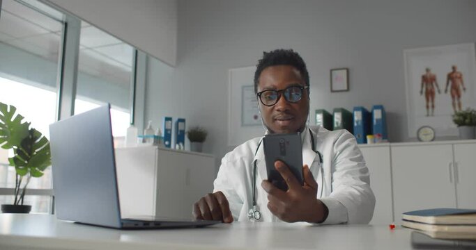 African md wearing white coat and stethoscope, communication with patient via video chat on phone