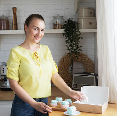 Kitchen, hobbies, people and cooking concept.Young woman pastry chef puts marshmallows in a box. Small home business.