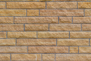 Natural rough textured stone block wall background in shades of beige, with large stone bricks of varying widths imparting an unusual stretcher bond pattern
