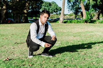 Naklejka na ściany i meble young Latin American millennial in a park pensive squatting and with a worried expression on his face.