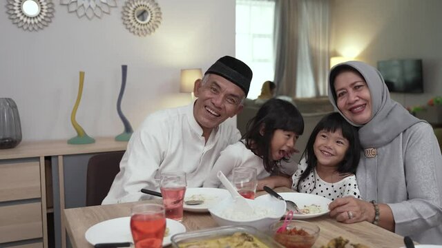 asian grandparents and grandchildren enjoying their time together looking at camera smiling having iftar dinner