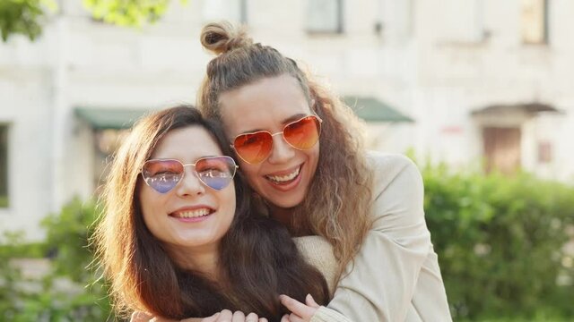 Lesbian girls hug, smile and show positive face emotions. Portrait of two young smiling hipster women friends wearing sunglasses of heart shape. LGBTQI, Pride Event, LGBT Pride Month, Gay Pride Symbol