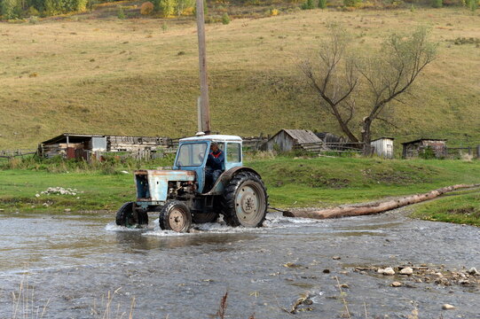 MTZ-80 tractor drags a tree trunk across the mountain river Yarovka in the taiga village of Generalka, Altai Krai