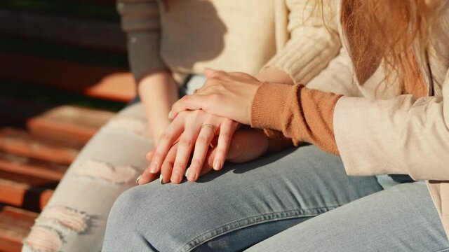 Close up oh female hands of two lesbian girls sitting outdoors. Caring young woman holding hand supporting her girlfriend or wife give empathy care love. LGBT Pride Month, Gay Pride Symbol
