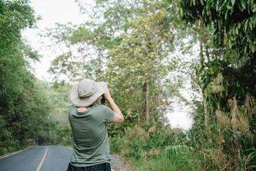 Back view of young asian woman with hiking hat looks through binoculars between a travel.