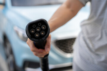 Unrecognizable Asian woman holding AC type 1 EV charging connector at EV charging station