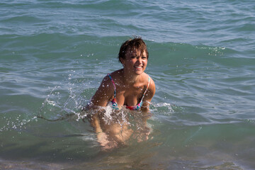 Schlanke Frau mit kurzen, dunklen Haaren, spritzt mit dem Wasser im Meer. Sie lacht und hat Spaß im Wasser. 