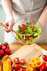 Beautiful young woman preparing delicious fresh vitamin salad. Concept of clean eating, healthy food, low calories meal, dieting, self caring lifestyle. Colorful vegetables, glass bowl. Close up