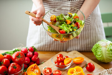 Beautiful young woman preparing delicious fresh vitamin salad. Concept of clean eating, healthy food, low calories meal, dieting, self caring lifestyle. Colorful vegetables, glass bowl. Close up