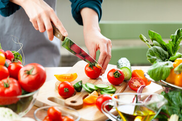 Beautiful young woman slicing red ripe tomato, preparing delicious fresh vitamin salad. Concept of...