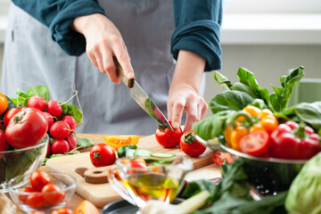 Beautiful young woman slicing red ripe tomato, preparing delicious fresh vitamin salad. Concept of clean eating, healthy food, low calories meal, dieting, self caring lifestyle. Close up